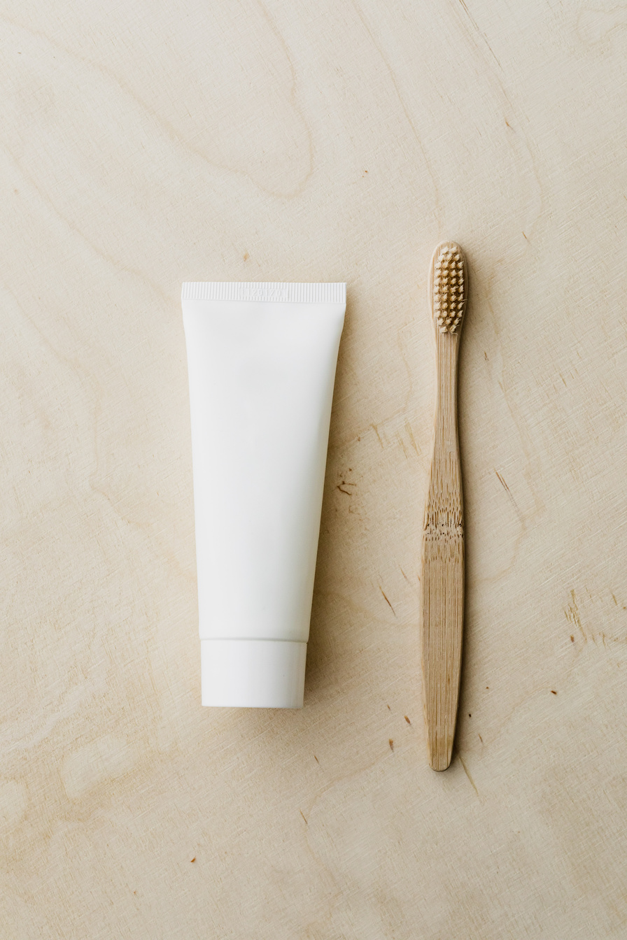 White toothpaste tube and bamboo toothbrush on wooden surface